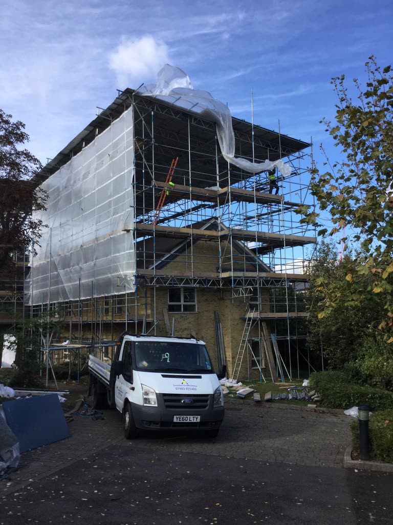 Scaffolded and sheeted to the full height of the front elevation, with the flats behind it occupied.